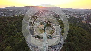 Budapest, Hungary - 4K flying away from the Statue of Liberty on Gellert Hill at sunset with Buda Hills