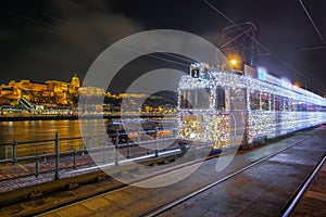 Budapest, Hungary - Festively decorated light tram fenyvillamos on the move with Buda Castle Royal Palace at Vigado square