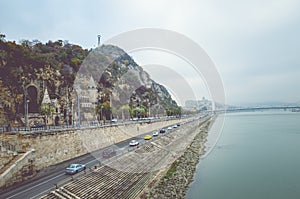 Budapest, Hungary - Nov 6, 2019: Gellert Hill Cave Church, Sziklatemplom. Liberty Statue on the top of the hill. Cars on the road