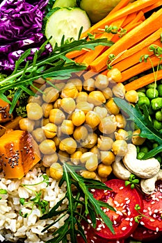 Bowl dish with brown rice, cucumber, tomato, green peas, red cabbage, chickpea, fresh lettuce salad and cashew nuts. Healthy balan