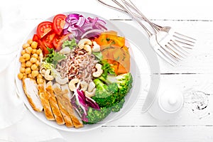 Buddha bowl dish with chicken fillet, brown rice, pepper, tomato, broccoli, onion, chickpea, fresh lettuce salad, cashew and walnu