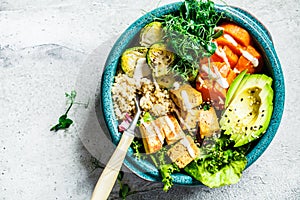 Buddha bowl with quinoa, tofu, avocado, sweet potato, brussels sprouts and tahini dressing, top view. Healthy vegan food concept