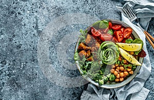 Buddha bowl salad with baked sweet potatoes, chickpeas, broccoli, tomatoes, greens, avocado, pea sprouts on light blue background