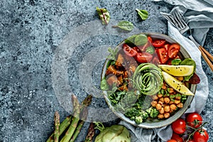 Buddha bowl salad with baked sweet potatoes, chickpeas, broccoli, tomatoes, greens, avocado, pea sprouts on light blue background