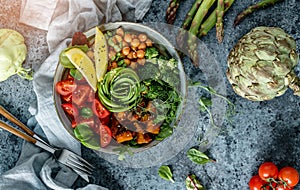 Buddha bowl salad with baked sweet potatoes, chickpeas, broccoli, tomatoes, greens, avocado, pea sprouts on light blue background