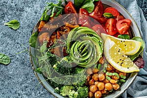 Buddha bowl salad with baked sweet potatoes, chickpeas, broccoli, tomatoes, greens, avocado, pea sprouts on light blue background