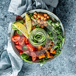 Buddha bowl salad with baked sweet potatoes, chickpeas, broccoli, tomatoes, greens, avocado, pea sprouts on light blue background