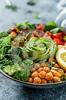 Buddha bowl salad with baked sweet potatoes, chickpeas, broccoli, tomatoes, greens, avocado, pea sprouts on light blue background