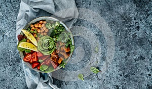 Buddha bowl salad with baked sweet potatoes, chickpeas, broccoli, tomatoes, greens, avocado, pea sprouts on light blue background