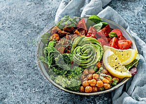 Buddha bowl salad with baked sweet potatoes, chickpeas, broccoli, tomatoes, greens, avocado, pea sprouts on light blue background