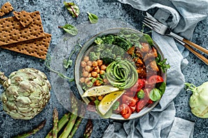 Buddha bowl salad with baked sweet potatoes, chickpeas, broccoli, tomatoes, greens, avocado, pea sprouts on light blue background