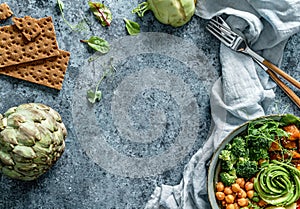 Buddha bowl salad with baked sweet potatoes, chickpeas, broccoli, tomatoes, greens, avocado, pea sprouts on light blue background