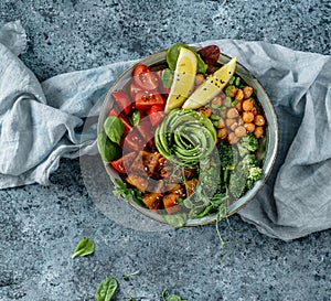 Buddha bowl salad with baked sweet potatoes, chickpeas, broccoli, tomatoes, greens, avocado, pea sprouts on light blue background