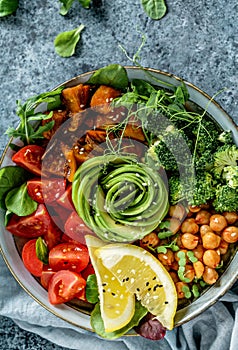 Buddha bowl salad with baked sweet potatoes, chickpeas, broccoli, tomatoes, greens, avocado, pea sprouts on light blue background