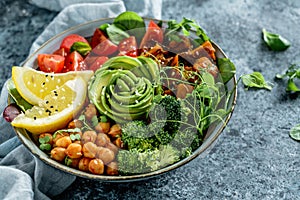 Buddha bowl salad with baked sweet potatoes, chickpeas, broccoli, tomatoes, greens, avocado, pea sprouts on light blue background