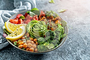 Buddha bowl salad with baked sweet potatoes, chickpeas, broccoli, tomatoes, greens, avocado, pea sprouts on light blue background