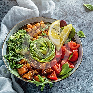 Buddha bowl salad with baked sweet potatoes, chickpeas, broccoli, tomatoes, greens, avocado, pea sprouts on light blue background