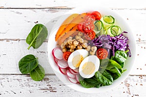 Buddha bowl salad with chickpeas, sweet pepper, tomato, cucumber, red cabbage kale, fresh radish, spinach leaves and boiled egg