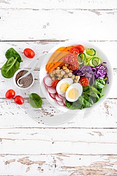 Buddha bowl salad with chickpeas, sweet pepper, tomato, cucumber, red cabbage kale, fresh radish, spinach leaves and boiled egg