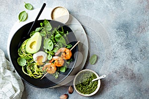 Buddha bowl with soft boiled egg, avocado, greens, zucchini noodles, grilled shrimps and pesto sauce. Low carb lunch bowl