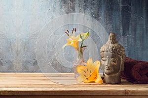 Buddha statue, flowers and towel on wooden table over dark background