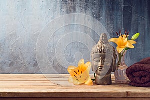 Buddha statue, flowers and towel on wooden table over dark background