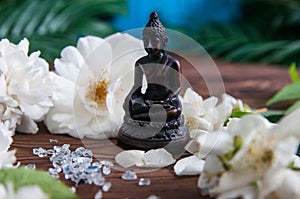 Buddha statue with white flowers, green leaves on wooden background. Concept of harmony, balance and meditation,