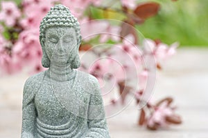 Buddha statuette against blurred blooming sakura branch as background with copy space