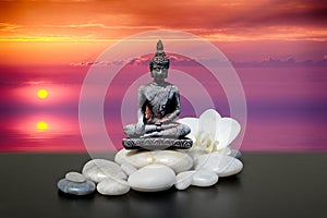 Buddha,zen stone,white orchid flowers.In the background sunrise over the sea