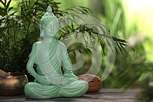 Buddhism religion. Decorative Buddha statue and singing bowl on wooden table outdoors, space for text