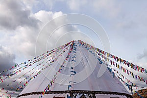 Buddhism symbol prayer flags on white yurt tent blue cloudy sky background.