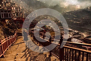 Buddhist nun walking down stairway at Larung gar in a warm and foggy morning time, Sichuan