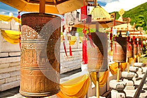 Buddhist prayer wheels in front of the temple jade-gold statue of the goddes Guanyin in the Nanshan park. On prayer wheels Mantra