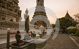 Buddhist statue standing in front of the ancient tiled Wat Arun temple, Bangkok, Thailand