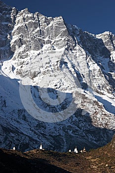 Buddhist stupas dwarfed by mountain cliff, Himalaya, Nepal