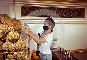 A Buddhist woman making merit at a temple and she wears a face mask to protect against the virus