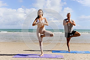 Buddy athlete woman, man doing yoga and stretching body on summer island beach, couple practicing yoga at seashore of tropical