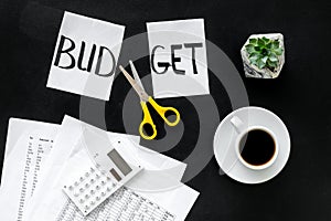 Budget reduce concept with accounting, sciccors and paper with cut word budget on black background top view