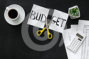 Budget reduce concept with accounting, sciccors and paper with cut word budget on black background top view mock-up