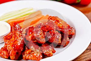 Buffalo chicken wings with blue cheese dip, carrots and celery sticks on white plate