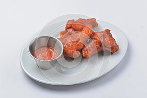 Buffalo chicken wings with tomato dip sauce. Served on a white plate over white background