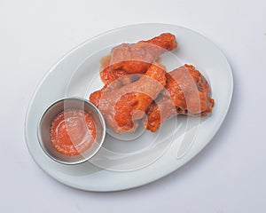 Buffalo chicken wings with tomato dip sauce. Served on a white plate over white background