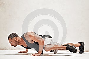 Buffed sportsman posing in a bright studio, while doing an exercise on the floor