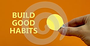 Build good habits symbol. Businessman holds yellow shining light bulb. Words `Build good habits`. Beautiful orange background.