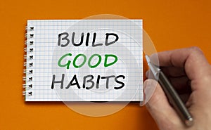 Build good habits symbol. Businessman writing words `Build good habits` on white note. Beautiful orange background. Business,