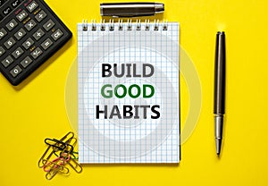 Build good habits symbol. Words `Build good habits` on white note. Yellow background, paper clips, metallic pen and calculator.