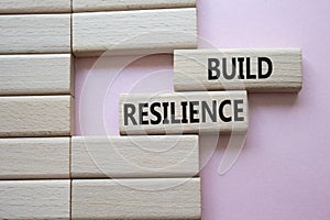 Build resilience symbol. Wooden blocks with words Build resilience. Beautiful pink background. Business and Build resilience