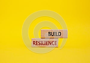 Build resilience symbol. Wooden blocks with words Build resilience. Beautiful yellow background. Business and Build resilience