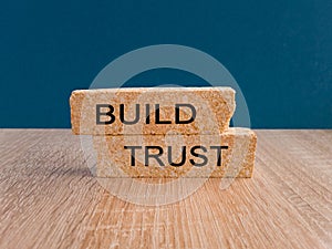 Build trust symbol. Concept words Build trust on brick blocks on a beautiful wooden table, dark blue background