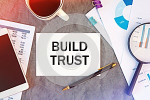 BUILD TRUST is written in a document on the office desk, coffee, diagram and smartfon